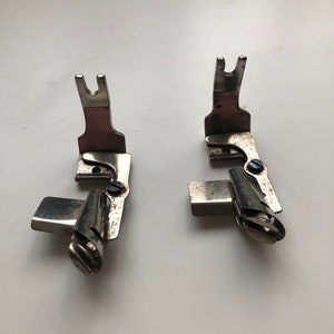 May include: Two silver sewing machine feet with a curved metal piece on the bottom. The feet are designed for sewing hems.