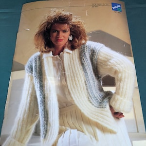 May include: A woman in a cream-coloured, long-sleeved cardigan with a light blue stripe design. The cardigan is paired with a white collared shirt and a pleated skirt. The image is from a vintage knitting pattern.