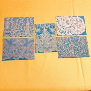 May include: Five white lace samples on blue backgrounds. The lace patterns are intricate and delicate.