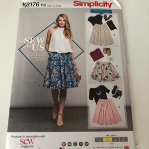 Könnte beinhalten: Ein Simplicity K8176 Schnittmusterumschlag für die Größen 14-22. Die Vorderseite zeigt ein weißes Neckholder-Top und einen blauen Rock mit Blumenmuster sowie weitere Varianten, darunter einen Spitzenrock, einen gemusterten Rock und einen rosa Rock.