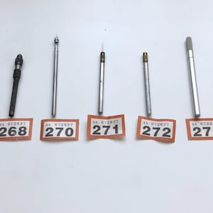 May include: A collection of nine metal and wood tools, each with a unique design. The tools are arranged in a row, with small orange labels beneath each one, displaying numbers from 266 to 295. The tools vary in color, including silver, black, and brown.