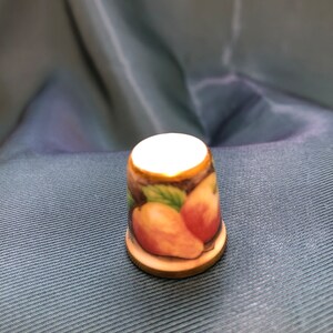 May include: A white porcelain thimble with a gold rim and a painted design of pears and leaves.