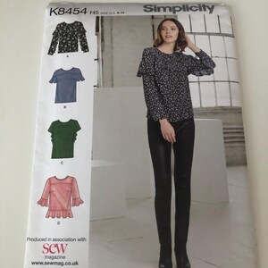 May include: A Simplicity sewing pattern envelope marked K8454 H5, showing illustrations of four blouse designs with ruffled sleeves. The front cover features a photograph of a floral print long-sleeve blouse with ruffled shoulders worn with black trousers.