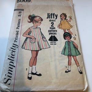 May include: Vintage Simplicity sewing pattern for a child's Jiffy dress, size 4. The pattern envelope shows illustrations of the dress designs, including a striped dress and a gingham dress. The envelope is cream-coloured with black text and illustrations.