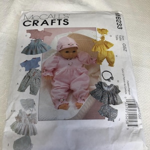 May include: A McCall's Crafts sewing pattern for doll clothes. The pattern packet shows a doll in a pink outfit and illustrations of different clothing items, such as dresses, trousers, and hats. The pattern number is M6233.