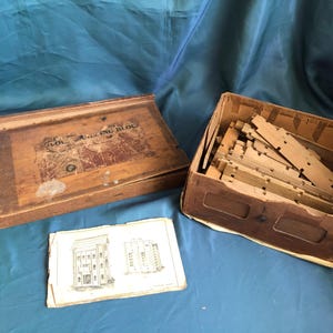 May include: A wooden box with the text "Model Building Block" on the lid. The box contains a set of wooden building blocks and a paper instruction sheet with two building plans.