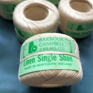 May include: A spool of white linen thread with a green label that reads "Barbour Campbell Threads Ltd. Linen Single Shoe Made in Northern Ireland".