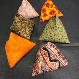 Könnte beinhalten: Sechs dreieckige Stoffkissen mit verschiedenen Mustern. Die Kissen sind aus verschiedenen Stoffen mit Blumen-, geometrischen und Blattmotiven gefertigt. Die Kissen sind in den Farben Grün, Orange, Gelb, Blau und Rot.