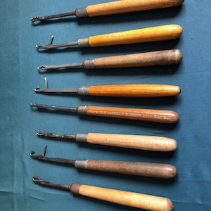 May include: Set of eight vintage wooden handled crochet hooks. The hooks are made of metal and have a variety of sizes. The handles are made of wood and have a natural finish. The hooks are in good condition and have been well-maintained.
