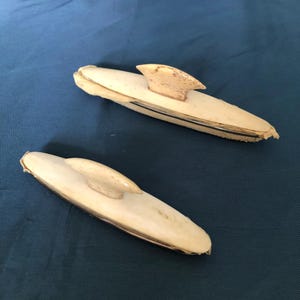 May include: Two ivory-colored, decorative, whale tooth carvings with a silver band around the middle. The carvings are shaped like a whale with a fin on the back.