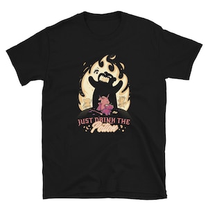 以下が含まれることがあります： 黒いTシャツに漫画のグラフィック。グラフィックは、炎の中のクマのような姿、小さなキャラクター、そしてピンク色のテキスト「JUST DRINK THE POTION」を特徴としています。デザインは気まぐれでファンタジーなテーマを持っています。