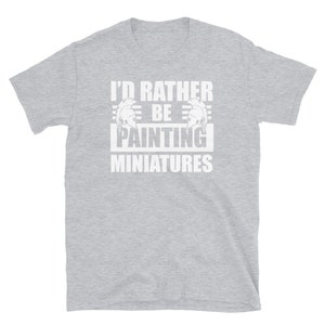 May include: Gray short-sleeved t-shirt with white text that reads "I'd rather be painting miniatures". The text is framed by two white helmet graphics.