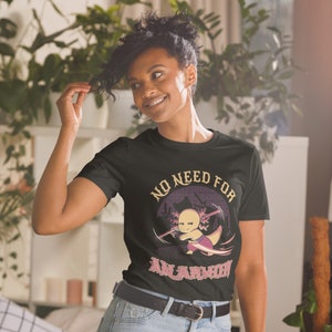 Könnte beinhalten: Ein schwarzes T-Shirt mit einem Aufdruck eines Axolotls, der ein Stirnband trägt und ein Schwert hält. Der Text "NO NEED FOR AN ARMOR" ist auf dem T-Shirt aufgedruckt.