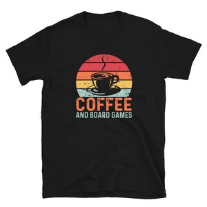 May include: Black t-shirt with a retro-style sunset graphic and a coffee cup. The text "Coffee and Board Games" is printed below the graphic.