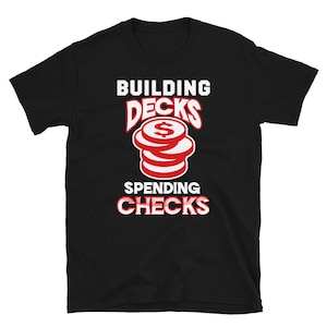 May include: Black t-shirt with red text that reads "Building Decks Spending Checks". The text is stylized with a stack of coins with a dollar sign on top.