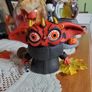 May include: A red and black Yoda figurine with horns and red eyes. The figurine is holding a lightsaber in its right hand.