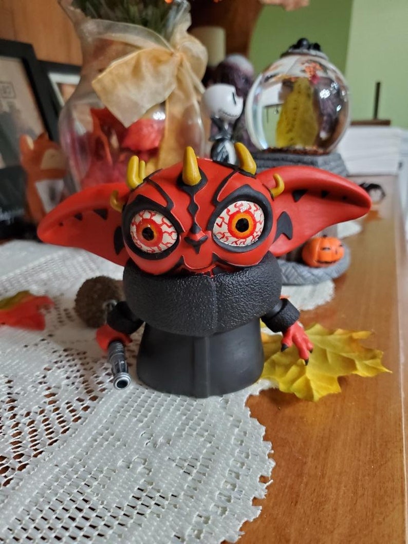 May include: A red and black Yoda figurine with horns and red eyes. The figurine is holding a lightsaber in its right hand.