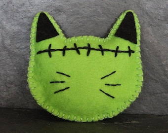 Peut inclure: Jouet pour chat en feutre vert avec des oreilles en feutre noir et des détails cousus, ressemblant à un monstre de Frankenstein.