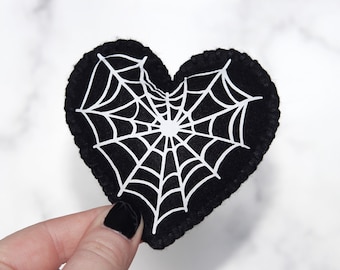 May include: A black felt heart-shaped ornament with a white spiderweb design.