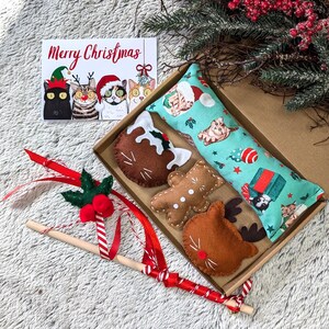 Può includere: Un set regalo di giocattoli per gatti a tema natalizio con un cuscino a stampa di gatto verde acqua e bianco, un omino di pan di zenzero, una renna e un biscotto a forma di gatto. Il set include anche una bacchetta di legno con nastro rosso e bianco e un rametto di agrifoglio.