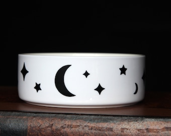May include: White ceramic bowl with a black crescent moon and stars design.