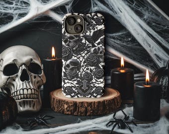 Op de afbeelding: Een witte iPhone-hoes met een zwart-wit ontwerp met schedels, rozen en een raaf. De hoes ligt op een houten oppervlak met een spin en kaarsen op de achtergrond.