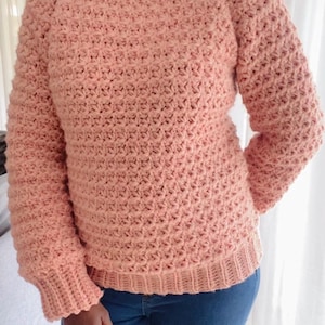 May include: A soft, pink crocheted jumper with long sleeves and a round neckline.