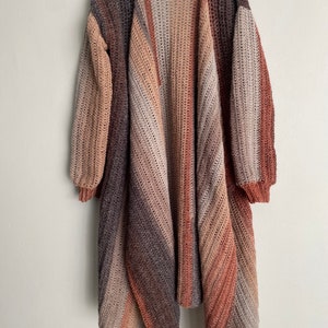May include: A long, open-front cardigan with a diagonal striped pattern in shades of brown, beige, and rust. The cardigan has a relaxed fit and long sleeves.