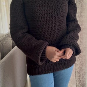 May include: A brown off-the-shoulder knitted sweater with long sleeves and a loose fit.
