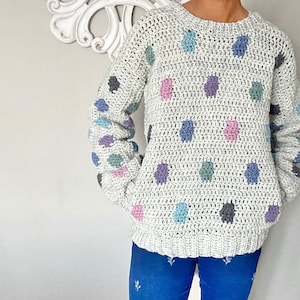 May include: A crocheted sweater with a light gray base and colorful polka dots. The sweater has a crew neck and long sleeves.