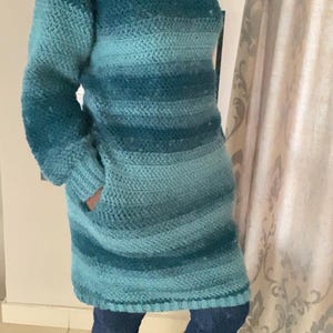 Pode incluir: Um vestido de tricô de crochê azul turquesa e azul escuro com bolsos. O vestido é usado com meias azuis escuras e botas pretas.