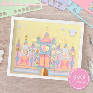 Peut inclure: Une œuvre d'art en papier superposé dans un cadre blanc, représentant un château stylisé avec des accents pastel rose, bleu, jaune et doré. Le design présente des formes géométriques, des engrenages, un motif soleil et lune et une arche centrale.