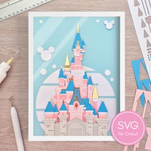 Può includere: Un'opera d'arte in carta a strati raffigurante un castello rosa e blu con dettagli dorati, su uno sfondo azzurro. L'opera è incorniciata in bianco, con sagome di Topolino e il testo "SVG for Cricut".