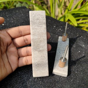 May include: Two white marble cabinet door pulls with silver screws. The pulls are rectangular and have a smooth, polished finish.