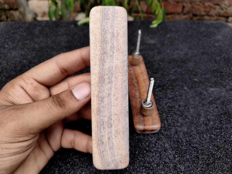 May include: A light-coloured wooden drawer pull held in a hand, with a rectangular shape and visible wood grain. Two smaller, similar drawer pulls with metal screws are also visible. The pulls are likely for furniture or cabinetry.