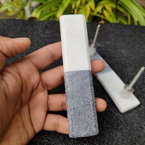 May include: Two white marble cabinet knobs with gray marble accents. The knobs have a silver screw in the back.