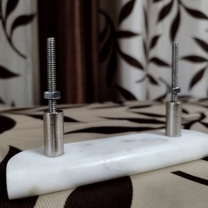May include: A white marble base with two silver metal screws protruding from the top.