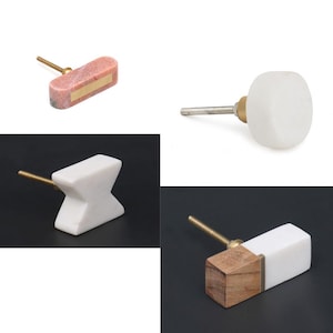 Könnte beinhalten: Vier verschiedene Arten von Schrankknöpfen aus Marmor und Holz. Die Knöpfe sind in verschiedenen Formen und Größen, darunter ein runder Knopf, ein rechteckiger Knopf und ein Knopf in Form eines X. Die Knöpfe sind alle weiß mit goldenen Akzenten.
