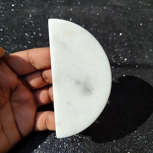May include: A white marble half-moon shaped coaster with a slightly grayed center.
