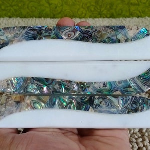 May include: Three white marble drawer pulls with iridescent abalone shell inlays. The pulls have a wavy design and are stacked on top of each other.
