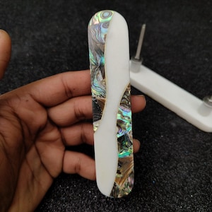 Op de afbeelding: Een rechthoekige ladegreep van witte, iriserende abalone-schelp met een zilveren schroef. De greep is glad en gepolijst.