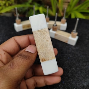 Pode incluir: Uma puxador de gaveta de madeira branca e marrom com acabamento liso e polido. A puxador é de forma retangular e tem uma borda ligeiramente arredondada.