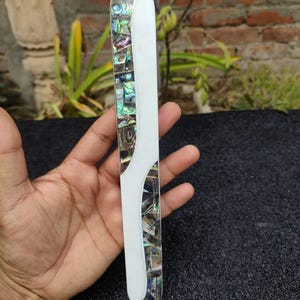 May include: A white and iridescent abalone shell decorative object with a smooth, polished surface. The object is long and narrow, with a curved shape.