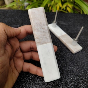 Può includere: Due tiretti per cassetti in marmo bianco con un accento in marmo marrone. I tiretti hanno una vite in metallo argentato sul retro.