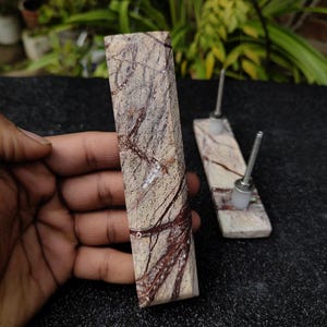 Può includere: Due pomelli per armadi in marmo marrone e bianco con una vite argentata. I pomelli hanno un motivo in pietra naturale.