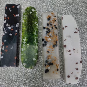 May include: Four rectangular resin bookmarks with different patterns. The bookmarks are black with white and red flecks, green with white flecks, white with black and gold flecks, and white with brown flecks.