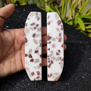 May include: Two white rectangular cabinet pulls with a speckled red and brown pattern.