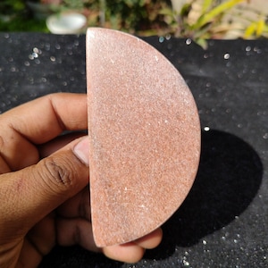 Op de afbeelding: Een halfronde vorm van roze en wit gevlekte steen. De steen is glad en gepolijst.