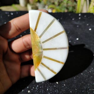 May include: A white and gold half-circle sunburst design made of mother of pearl. The sunburst has a white background with gold inlay.