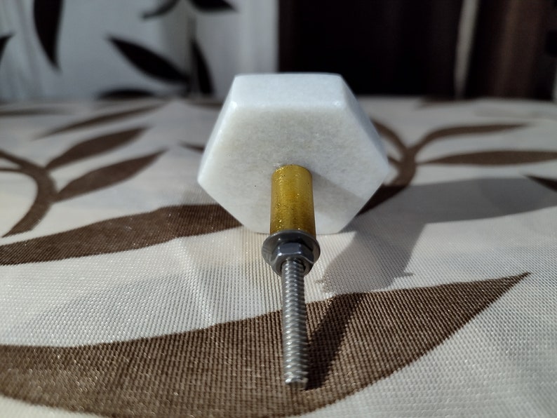 Pode incluir: Puxador de arm&aacute;rio hexagonal branco em m&aacute;rmore com haste dourada e parafuso prateado. O puxador &eacute; projetado para m&oacute;veis e tem uma est&eacute;tica moderna e minimalista. O hardware &eacute; adequado para gavetas e portas.